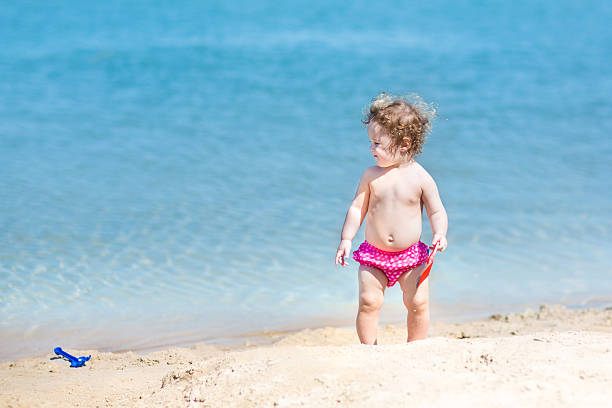 Cute funny baby girl with curly hair playing on beach Cute funny baby girl with curly hair playing in sand on a beach backside for a girl on the beach stock pictures, royalty-free photos & images