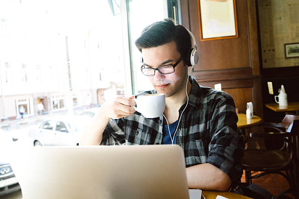 Cheerful Young Man Using Laptop In Coffee Shop Cheerful young man using laptop in coffee shop. russian culture audio stock pictures, royalty-free photos & images