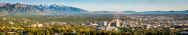 Salt Lake City sweeping panoramic vista across downtown mountains Utah Blue skies and snow capped mountains above the landmarks of Salt Lake City, from the leafy suburbs and University campus to the monument dome of the State Capitol and the ornamental spires of the Mormon Temple surrounded by the skyscrapers of downtown, Utah, USA. ProPhoto RGB profile for maximum color fidelity and gamut. salt lake city mormon temple utah photos stock pictures, royalty-free photos & images