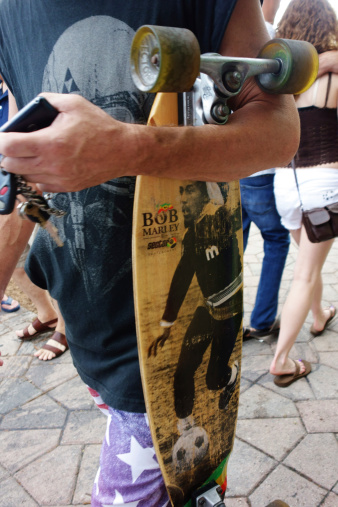 Lake Worth, Florida, USA - February 23, 2014: A young man among the crowd of spectators at the Lake Worth Street Painting Festival carries a Bob Marley skateboard and his cell phone. The festival attracts thousands of visitors and features hundreds of artists who cover the streets with chalk paintings.