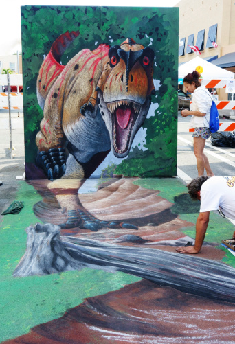 Lake Worth, Florida, USA - February 23, 2014:Two artists put the finishing touches on a combined street art drawing and billboard mural at the Lake Worth Street Painting Festival. The Lake Worth Street Painting Festival features hundreds of artists who cover the streets with chalk paintings. Movies were the theme of this year's festival and this artwork depicts a scene from Jurassic Park.
