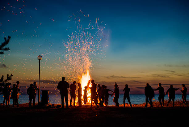 pessoas descansando perto de big fogueira ao ar livre - bonfire people campfire men - fotografias e filmes do acervo