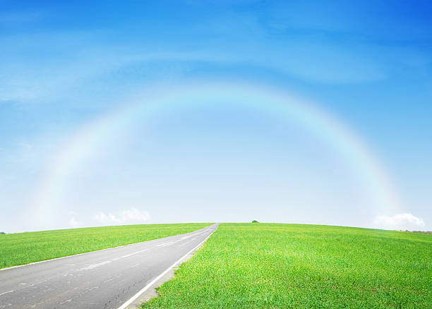The Perspective line from road, grass on wayside and rainbow on the blue sky. never end to go concept. image for background, wallpaper and backdrop.