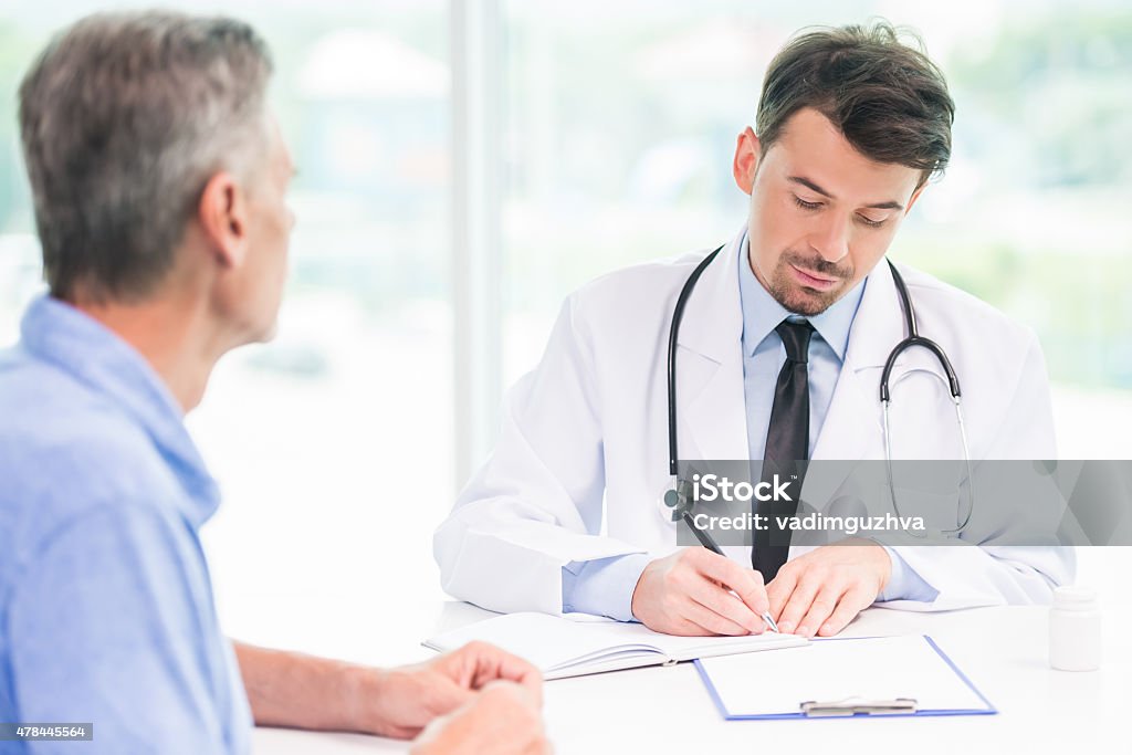 Doctor and patient Male doctor talking with patient and writing down recipe for medicine. 2015 Stock Photo