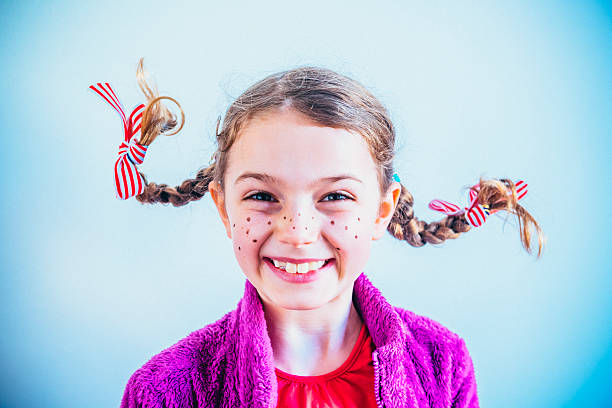 Young girl dressed up as Pippi Longstocking with bows and plaits sticking out and painted on freckles.
