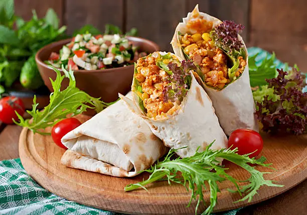 Burritos wraps with minced beef and vegetables on a wooden background