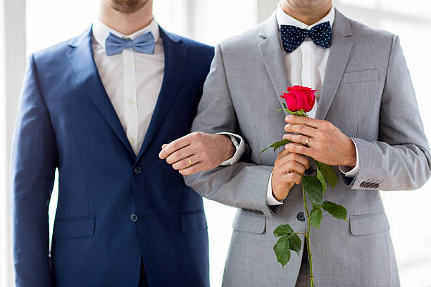close up of happy male gay couple holding hands people, homosexuality, same-sex marriage and love concept - close up of happy male gay couple with red rose flower holding hands on wedding civil partnership stock pictures, royalty-free photos & images