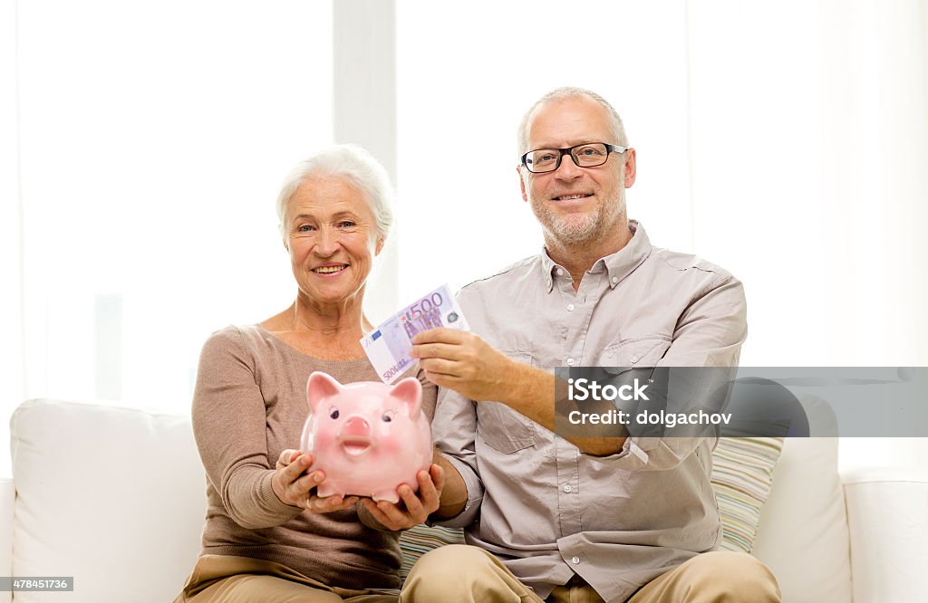 senior couple with money and piggy bank at home family, savings, age and people concept - smiling senior couple with money and piggy bank at home Couple - Relationship Stock Photo