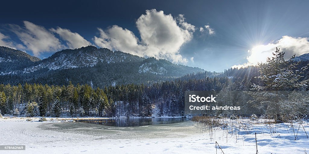 small frozen lake in austrian alps with sun shining small frozen lake in austrian alps with sun shining through clouds Blizzard Stock Photo