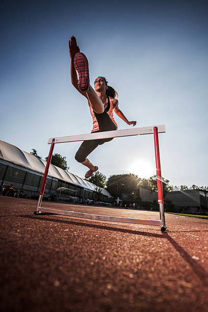 poniżej widok młodej kobiety skakać, biec przez płotki. - hurdling hurdle competition endurance zdjęcia i obrazy z banku zdjęć