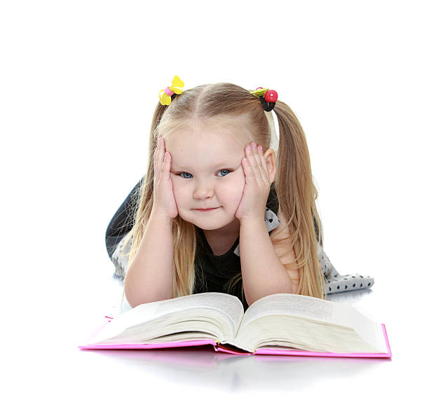 istock Chubby little blonde girl reading a book lying on the 478485836