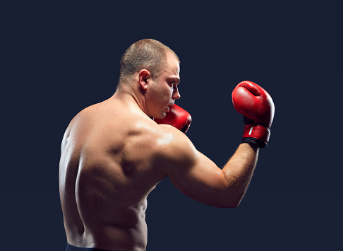 Young boxer in red gloves boxing over black background