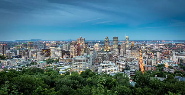 A DSLR panoramic picture of Montreal Cityscape at sunset. The St-Lawrence river is in the background of the picture. Downtown Montreal and Old Montreal are in the foreground and illuminated. It is a beautiful fall day and the sky is blue and clouded. The natural light of the sunset is making the city look luminous. 