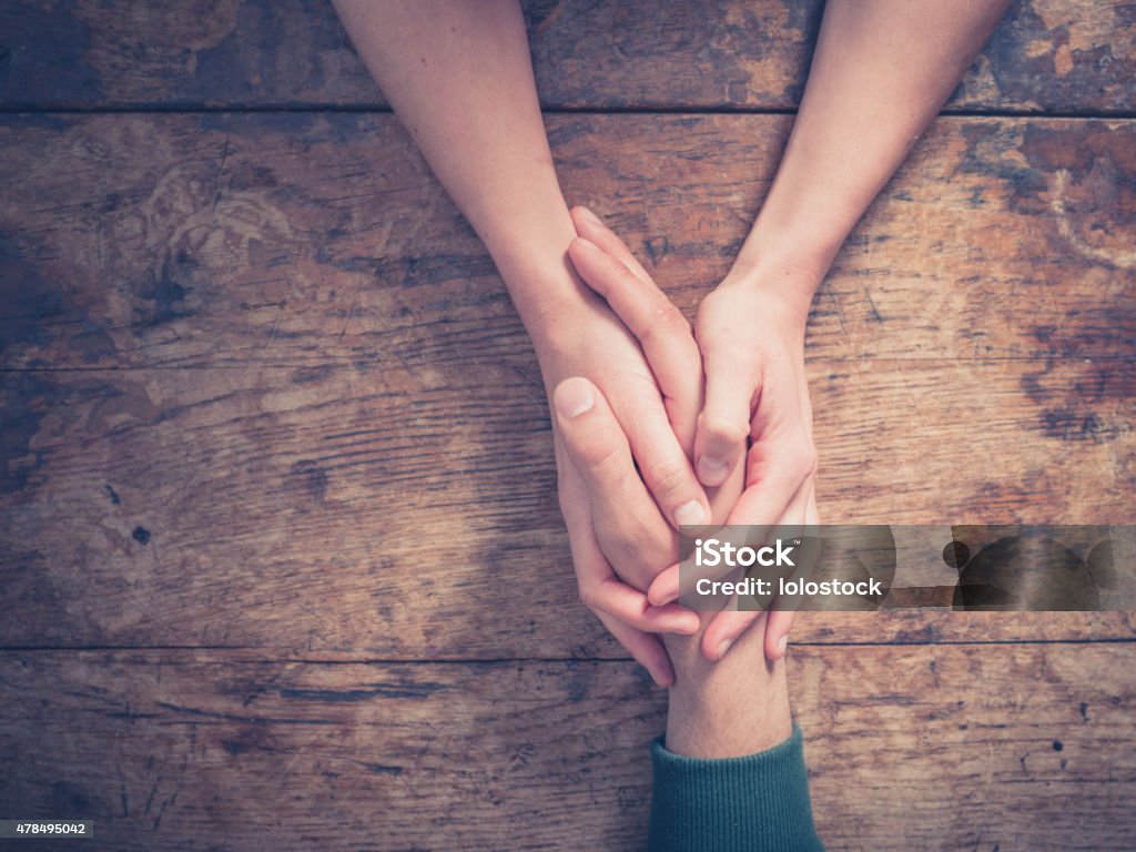 Man and woman holding hands at a table Close up on a man and a woman holding hands at a wooden table Consoling Stock Photo