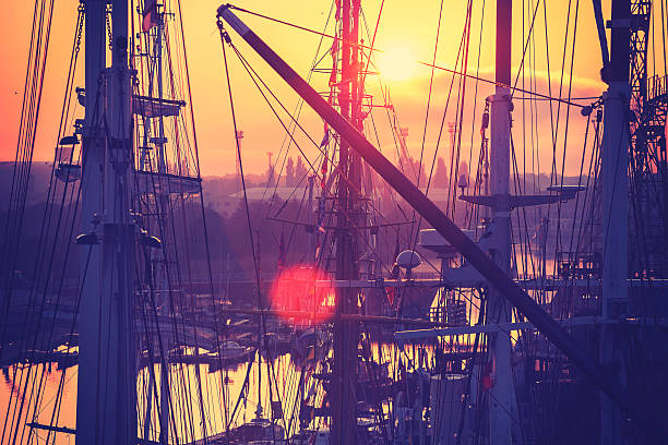 Vintage toned sunrise over harbor, sailing boats masts, lens flare effect.