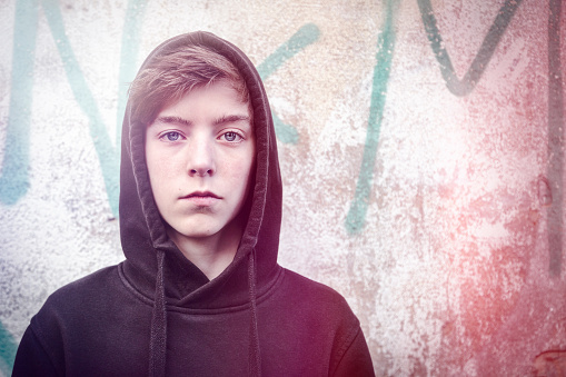 portrait of a teenage boy with black hoodie in front of a graffiti