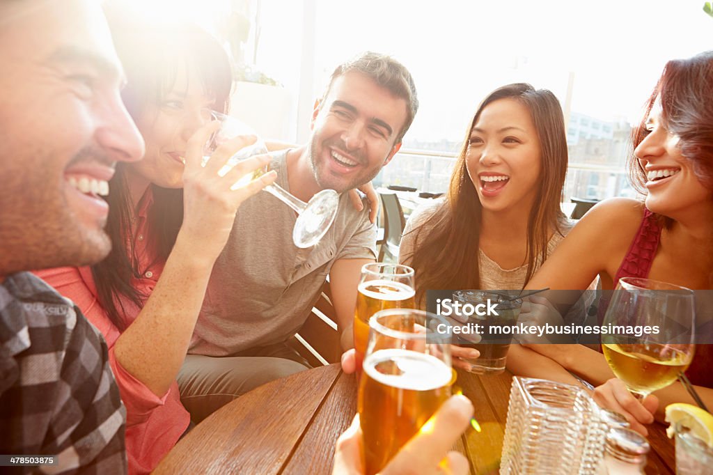 Group Of Friends Enjoying Drink At Outdoor Rooftop Bar Group Of Friends Enjoying Drink At Outdoor Rooftop Bar Laughing And Chatting Around Table. Beer - Alcohol Stock Photo