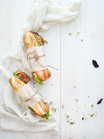 Sandwiches with beef, fresh vegetables and herbs over white wood backdrop, top view, copy space