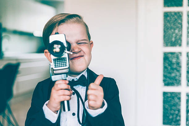 Thumbs up from boy shooting video with retro camera Boy with blond hair shows a thumbs up sign while shooting a video with an old analog 8 mm retro camera. The boy wears a tuxedo with a bow tie. tuxedo photos stock pictures, royalty-free photos & images