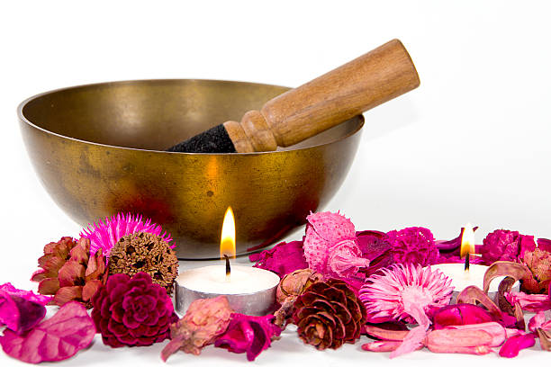 Studio shot of a tibetan bowl, some pink flowers and candles, over white background.