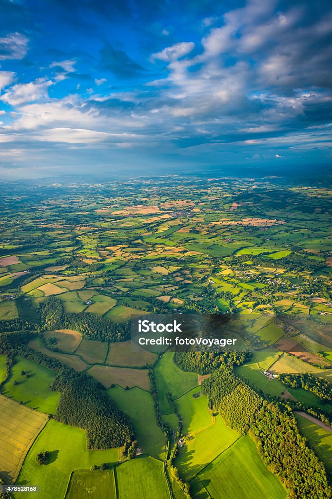 Aerial vista across green summer landscape under big country skies Big skies, dappled sunlight and dramatic clouds above an idyllic patchwork summer landscape of rolling hills, lush green farmland and country villages. ProPhoto RGB profile for maximum color fidelity and gamut. UK Stock Photo