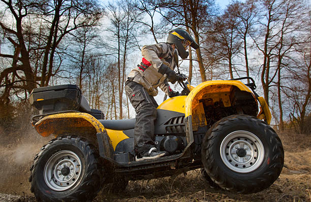 Dirt spinning of the ATV quad bike wheels Horizontal motion portrait of a man in gray sport jacket and safety helmet and goggles driving mud-covered yellow ATV 4x4 quad bike with dirt spinning of the wheels. quadbike photos stock pictures, royalty-free photos & images