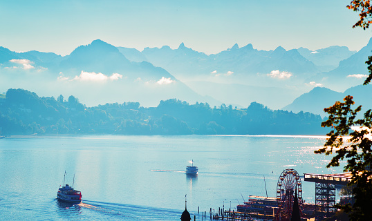 Lake Lucerne, Switzerland, on a sunny October morning with ferry boats. mist and fog covers the alpine background. Ferris wheel and piers in the foreground.