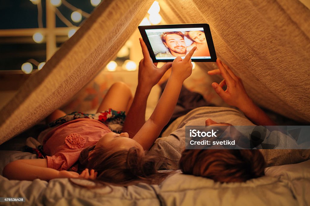 Father and daughter enjoying at home. Father and daughter enjoying at home. Lying on bed at night in do it yourself tent and using digital tablet together. Taking selfies and watching photos. Family Stock Photo