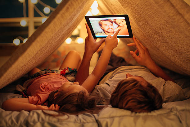 Father and daughter enjoying at home. Father and daughter enjoying at home. Lying on bed at night in do it yourself tent and using digital tablet together. Taking selfies and watching photos. tent photos stock pictures, royalty-free photos & images