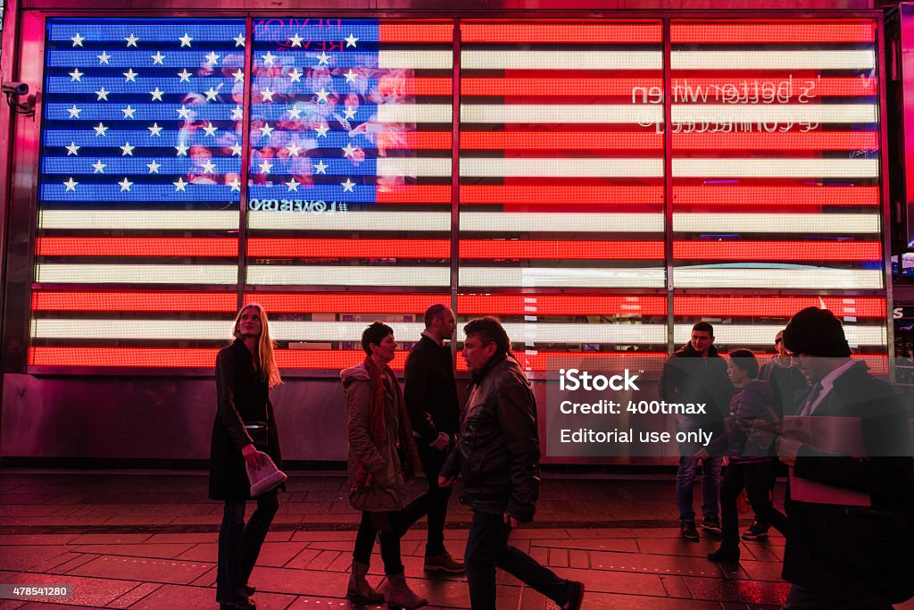 American Flag New York, USA - March 26, 2015: A giant illuminated American flag with tourists passing by in Times Square.  2015 Stock Photo