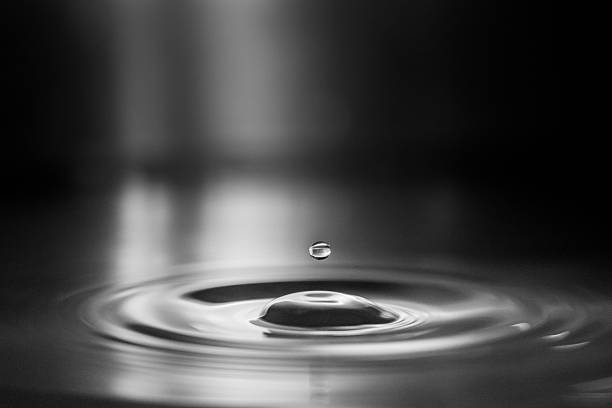 Macro monochrome image of suspended water droplet over rippled surface stock photo