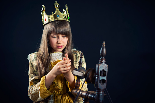 Sleeping beauty after pricking her  finger on spindle Little princess sitting by the spindle looking at her hurt finger. The girl is wearing a crown and a princess dress.