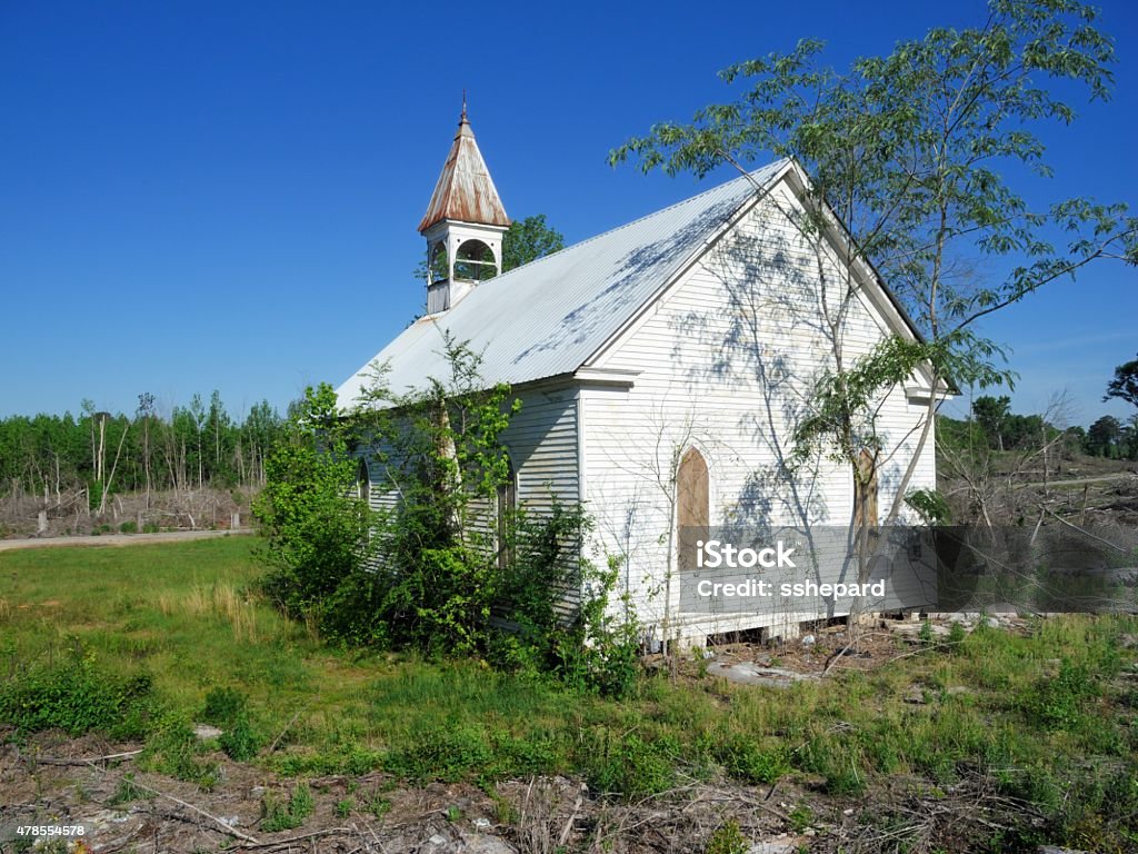 Abandoned church in demolished forest Photograph of small chapel that is abandoned and boarded up.  Church is located in field with fallen trees and weeds.  Church building is being overgrown by trees and weeds.  Horizontal composition image with copy space above. 2015 Stock Photo