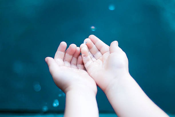 Children's hands grabbing water drops, turquoise/blue background.
