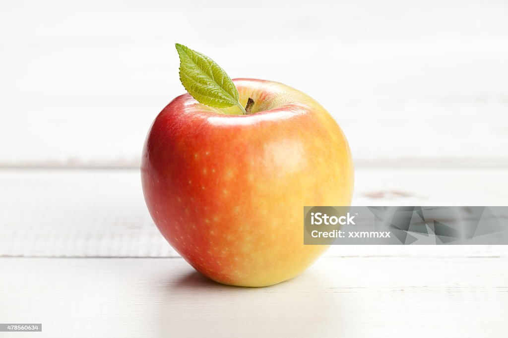 Colorful apple with leaf on white table Colorful apple with leaf on white wooden table. This file is cleaned and retouched. 2015 Stock Photo