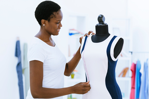 African woman, fashion designer working in her office. Standing and measuring on dressmaker model.