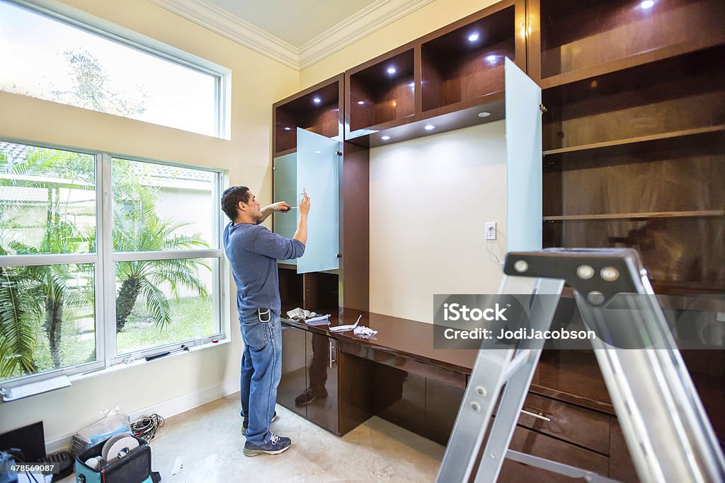 Home office installation A worker is assembling parts of a home office wall unit inside a home.  rr Customized Stock Photo