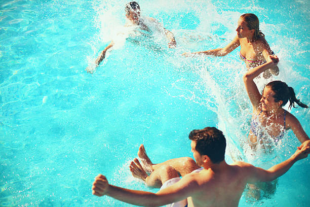 Friends enjoying their vacation by jumping into swimming. They're spalshing all over. There are two guys and two girls jumping in circle. They left some nice copy space for you.