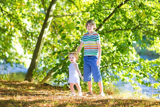 istock Cute school boy holding baby sister playing at river shore 478584123