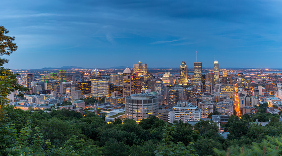 A DSLR panoramic picture of Montreal Cityscape at sunset. The St-Lawrence river is in the background of the picture. Downtown Montreal and Old Montreal are in the foreground and illuminated. It is a beautiful fall day and the sky is blue and clouded. The natural light of the sunset is making the city look luminous. 