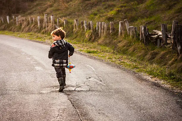 Small boy runs along the road, glancing over shoulder. 