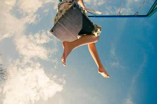 barefoot young woman in dress on swing outdoor in park warm spring day