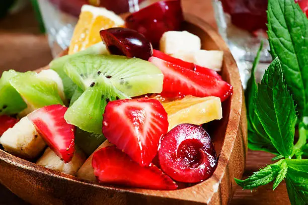 Dietary mixed fruit salad with fruit and berries in a wooden bowl, selective focus