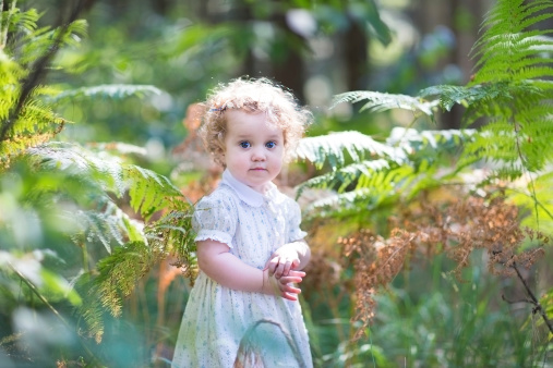 Adorable curly baby girl wearing a white dress playing in a sunny autumn park