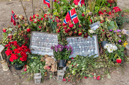 Oslo, Norway - September 17, 2011: After the 2011 Norway attacks on July 22 where a total of 77 people lost their life, lots of flowers, candles and flags were laid in front of the Oslo Cathedral by people bemoaning the victims. By mid-September much of the (withered) flowers had been removed, but the flowers, candles, flags, teddy bear, and framed pictures of the victims (from a newspaper) in the picture, were kept as a memorial. 