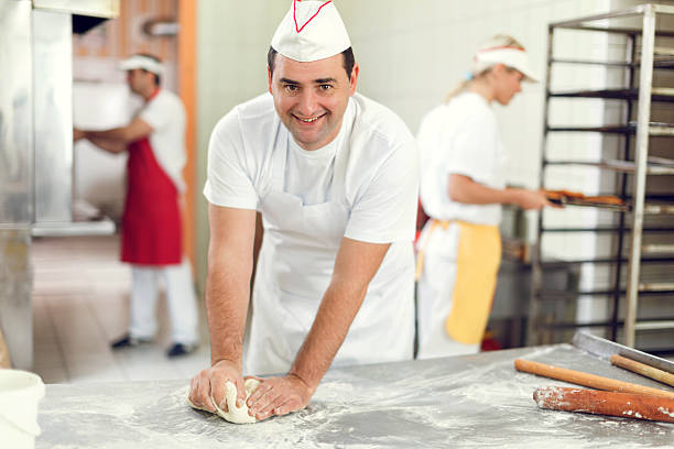 istock Smiling man kneading dough in bakery and looking at camera. 478619778