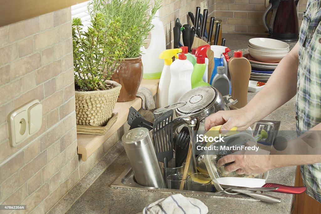 Man washing dirty dishes in the kitchen sink Man washing dirty dishes in the kitchen sink. Domestic cleaning up after the party. 2015 Stock Photo