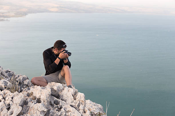 istock Photographer sitting stone cliff above lake sea. 478623670