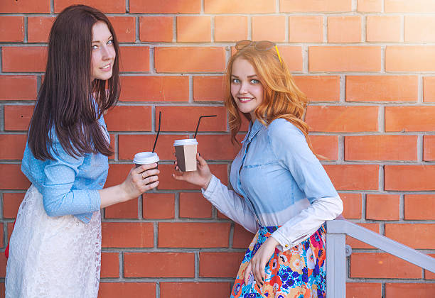 deux jeunes filles avec des tasses de café parler - back against the wall photos et images de collection