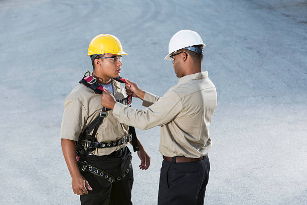 Workers, putting on safety harness Multi-ethnic workers (20s, 30s) with hardhats, putting on safety harness. safety harness photos stock pictures, royalty-free photos & images